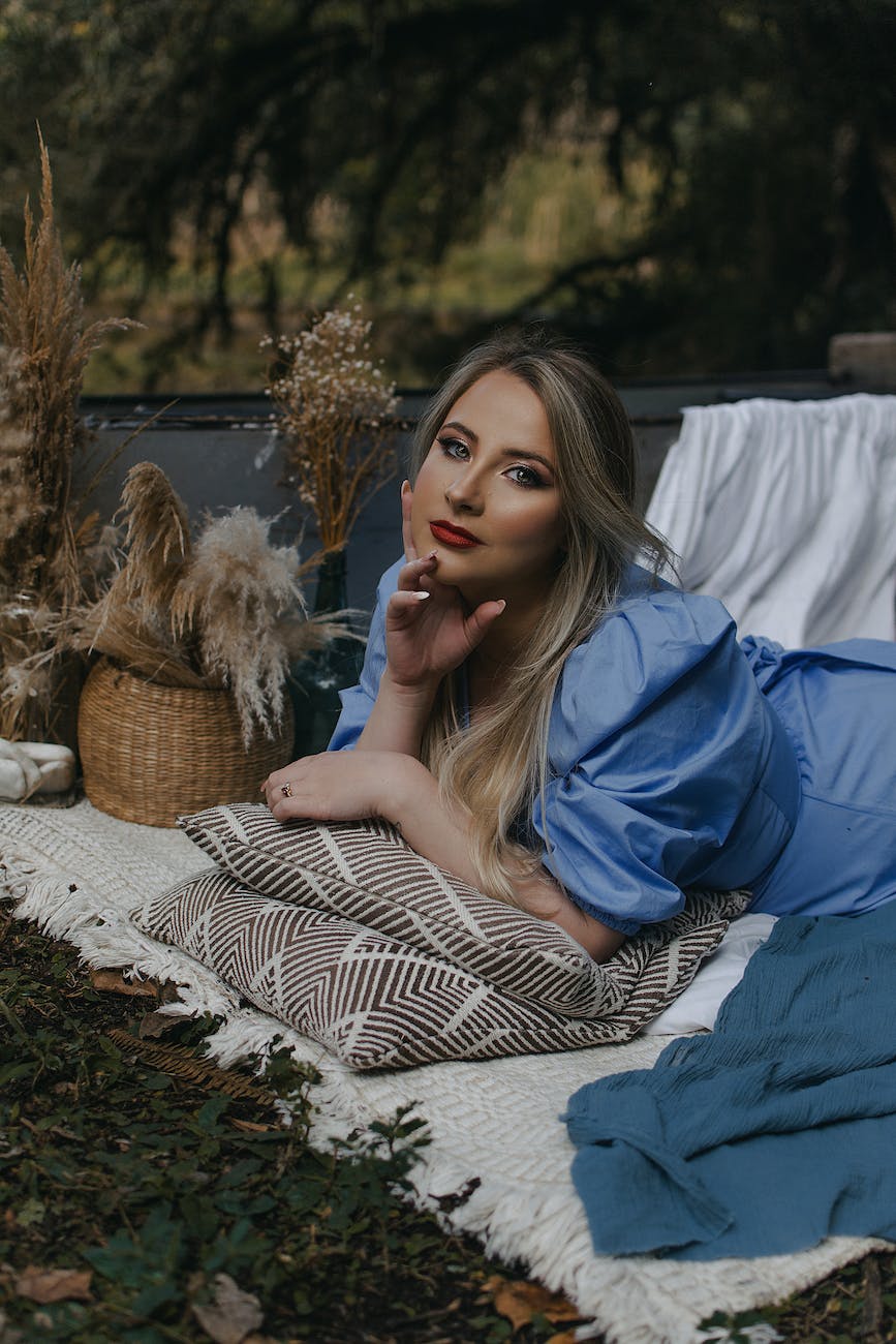 a beautiful woman in blue blouse lying on white picnic blanket while seriously looking at the camera